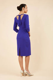 brunette model wearing diva catwalk wimpole a-line flattering dress with lowered v-neck at the back and tie detail and three quarter sleeve and and widened skirt with vent  in spectrum indigo back