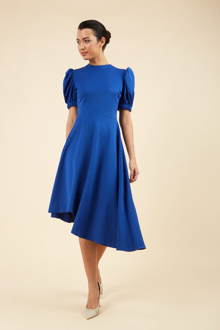 brunette model wearing diva catwalk ola swing dress with puffed oversized sleeves and asymmetric swing skirt with rounded high neck in blue front