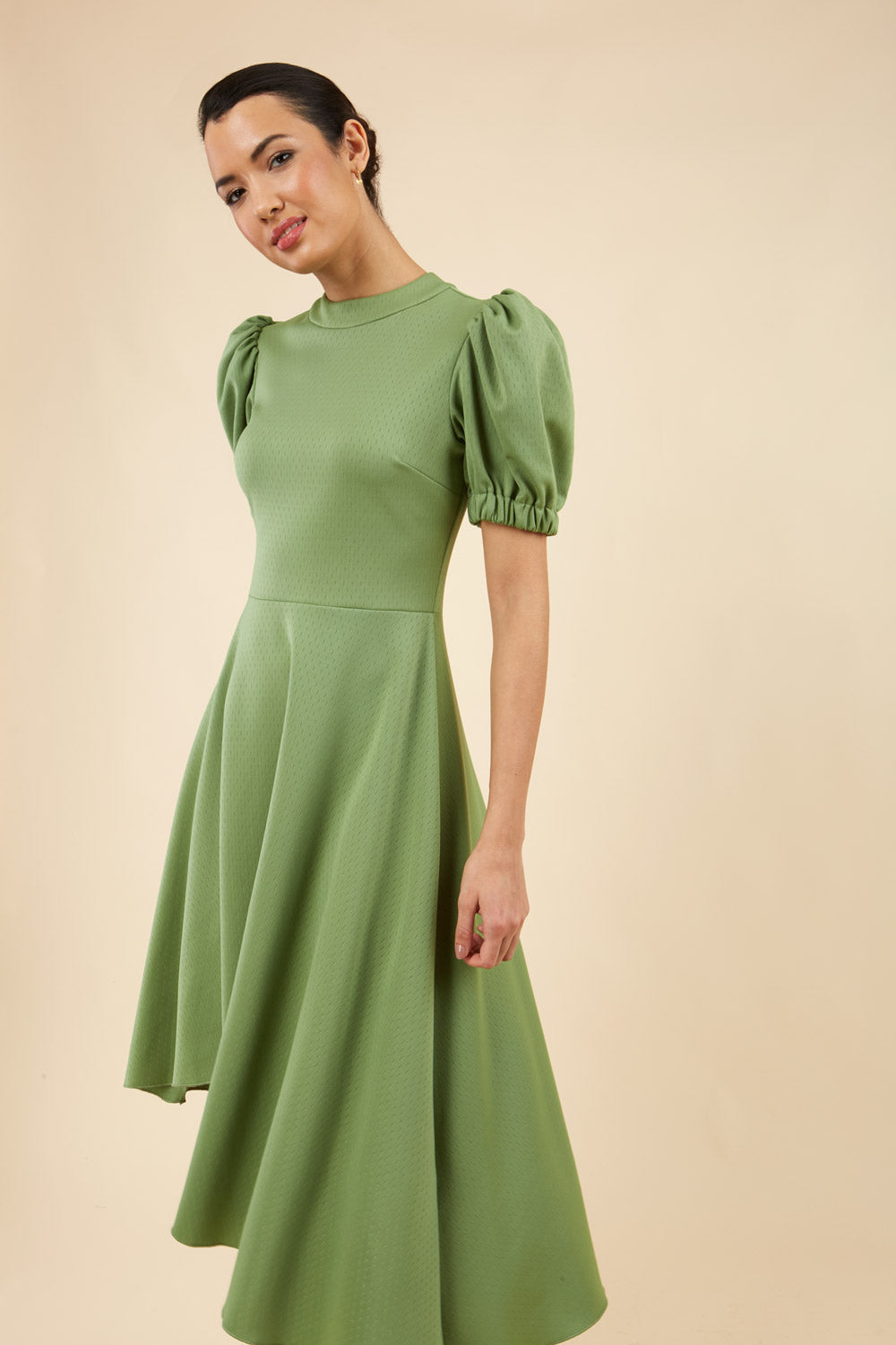 brunette model wearing diva catwalk ola swing dress with puffed oversized sleeves and asymmetric swing skirt with rounded high neck in green front