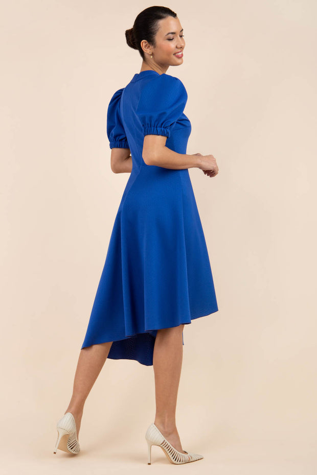 brunette model wearing diva catwalk ola swing dress with puffed oversized sleeves and asymmetric swing skirt with rounded high neck in blue back