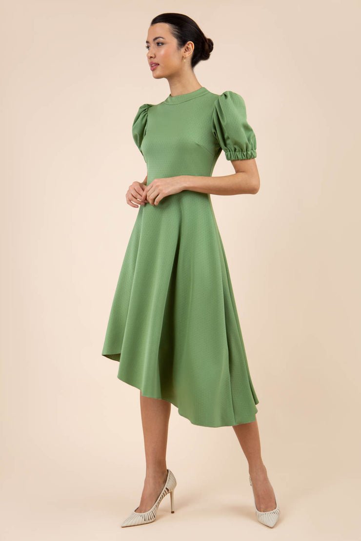 brunette model wearing diva catwalk ola swing dress with puffed oversized sleeves and asymmetric swing skirt with rounded high neck in green front