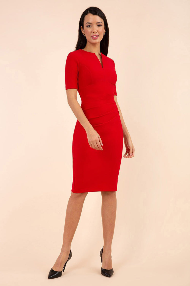 blonde model is wearing diva catwalk lydia short sleeve pencil fitted dress in true red colour with rounded neckline with a slit in the middle front
