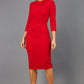 brunette model wearing diva catwalk elodie pencil fitted dress with rounded neckline and button detail and three quarter sleeve with pleating across the body from side triangle detail in scarlet red front