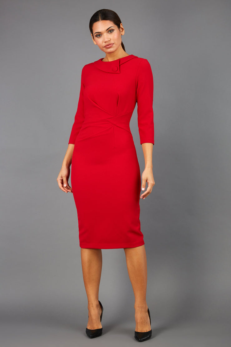 brunette model wearing diva catwalk elodie pencil fitted dress with rounded neckline and button detail and three quarter sleeve with pleating across the body from side triangle detail in scarlet red front