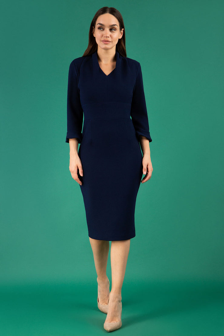 brunette model wearing diva catwalk adriana pencil dress with low v-neck and pleating around shoulders with three quarter sleeve detailed on end and wide waistband in navy front