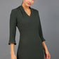 brunette model wearing diva catwalk adriana pencil dress with low v-neck and pleating around shoulders with three quarter sleeve detailed on end and wide waistband in obsidian green front