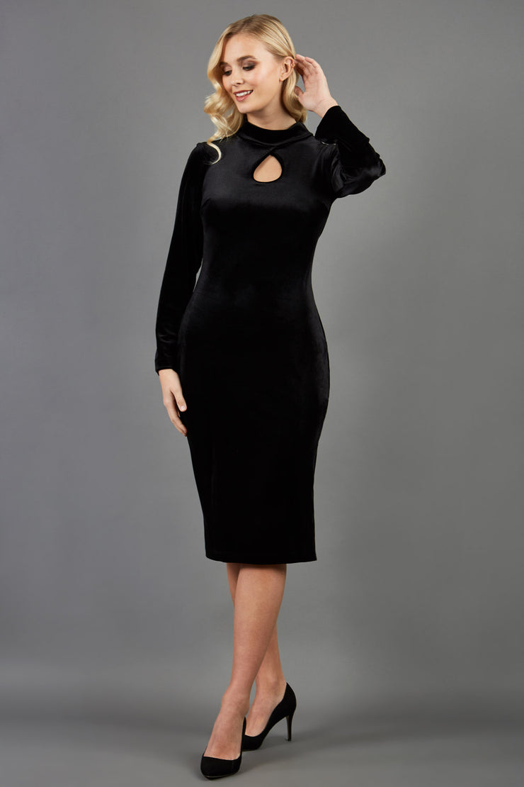 brunette model wearing diva catwalk clipper pencil skirt dress velvet sleeved style with a keyhole detail and high neck and split on a side of the skirt in colour black front