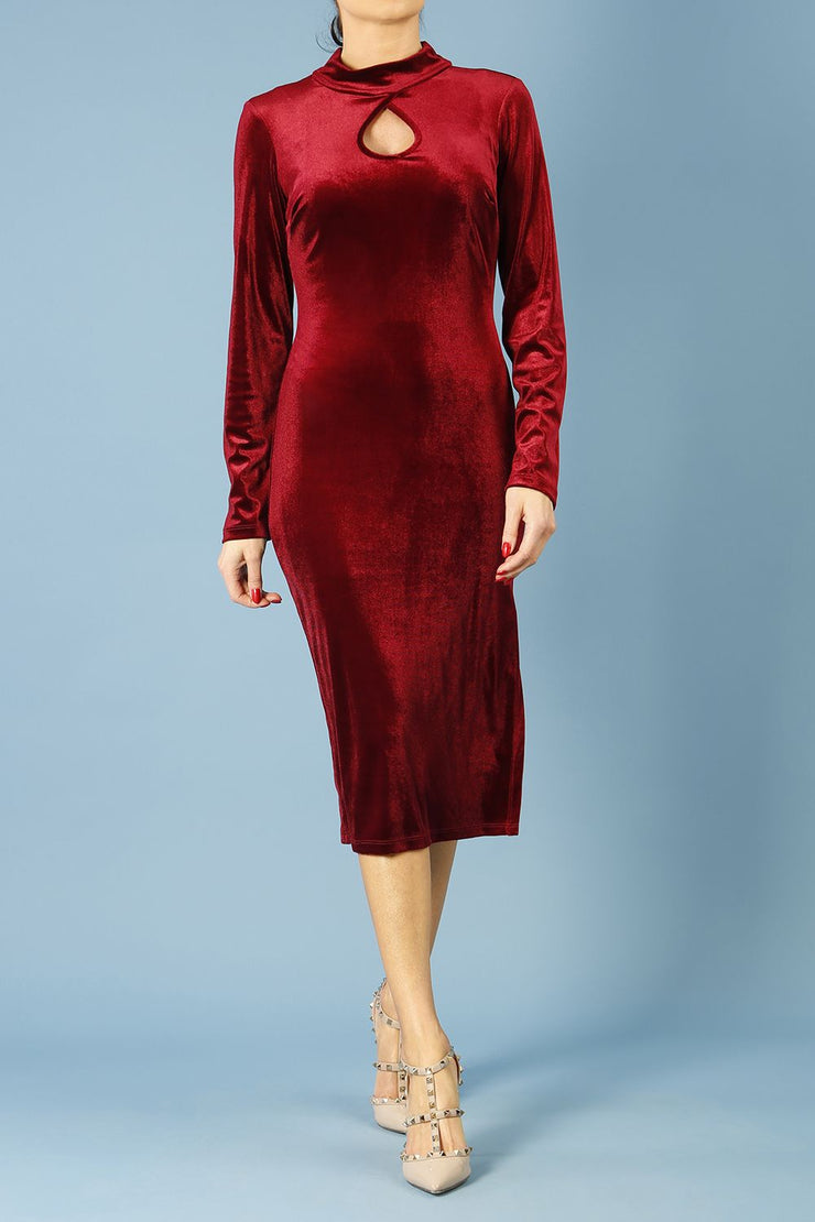brunette model wearing diva catwalk clipper pencil skirt dress velvet sleeved style with a keyhole detail and high neck and split on a side of the skirt in colour burgundy front