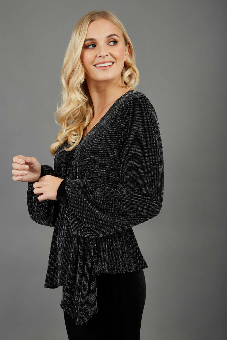 Blonde hair model is wearing a jersey sparkle v neck wrap blouse with bishop sleeve detail and bow on a side side image