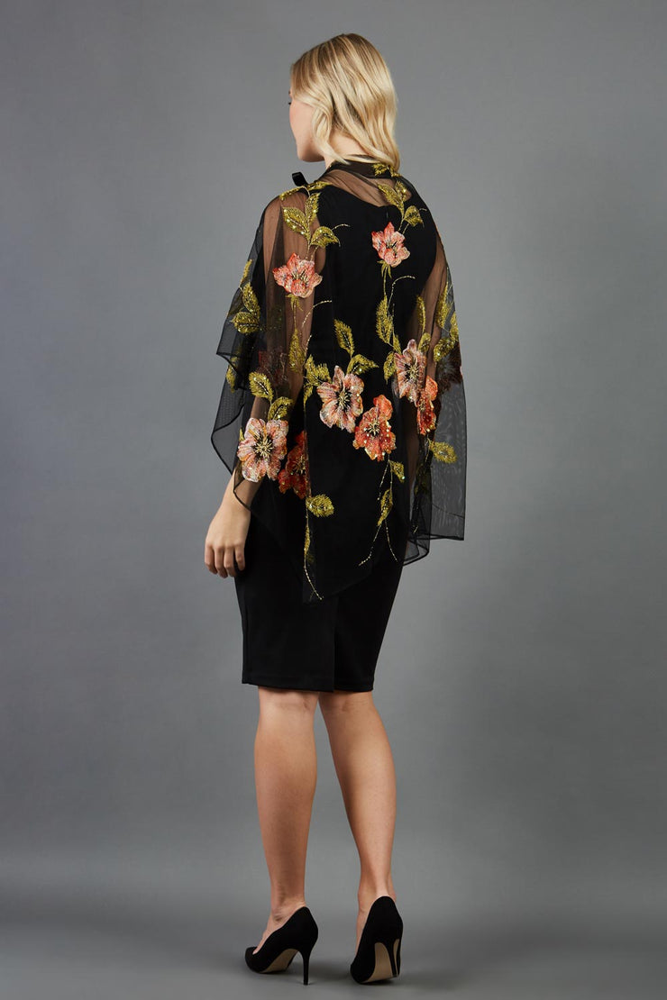 blonde model is wearing diva catwalk valparaiso black floral cape paired with diva sleeveless pencil black dress back