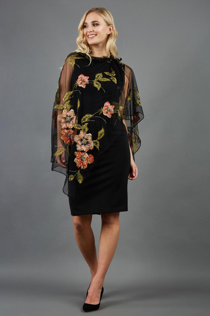 blonde model is wearing diva catwalk valparaiso black floral cape paired with diva sleeveless pencil black dress front