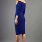 blonde model is wearing diva catwalk charisma dress odd shoulder design with pleated detail down the front and flower detail on a side in navy blue back