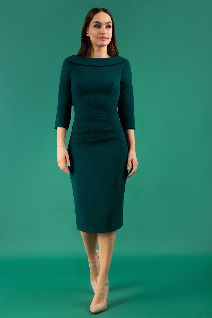 A brunette model is wearing a round neckline pencil dress with pleating on the tummy area in forest green front image