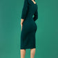 A brunette model is wearing a round neckline pencil dress with pleating on the tummy area in forest green back image