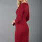 model is wearing a red pencil three quarter sleeve dress with assymetric neckline and pleating around tummy area back wine colour
