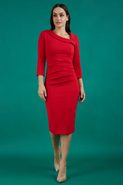 Brunette model is wearing a red pencil three quarter sleeve dress with assymetric neckline and pleating around tummy area
