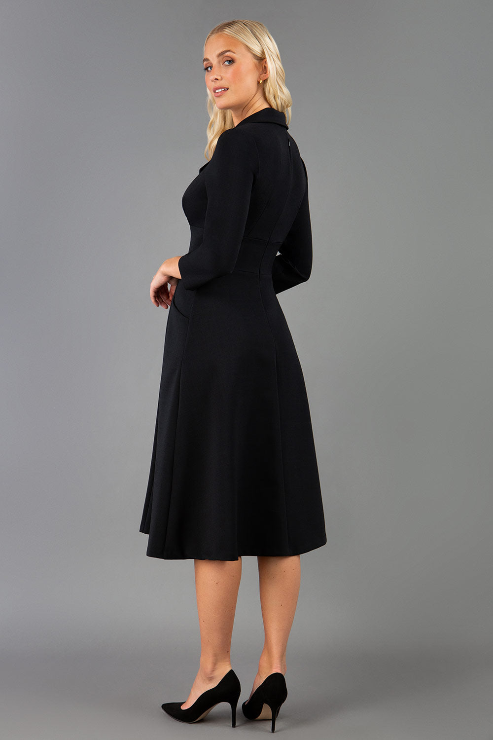 A blonde model is wearing a swing black three quarter sleeve dress with oversized collar and pockets in the skirt  