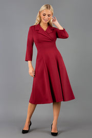 A blonde model is wearing a swing wine three quarter sleeve dress with oversized collar and pockets in the skirt  