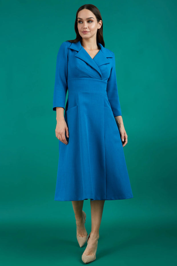 A brunette model is wearing a swing teal three quarter sleeve dress with oversized collar and pockets in the skirt
