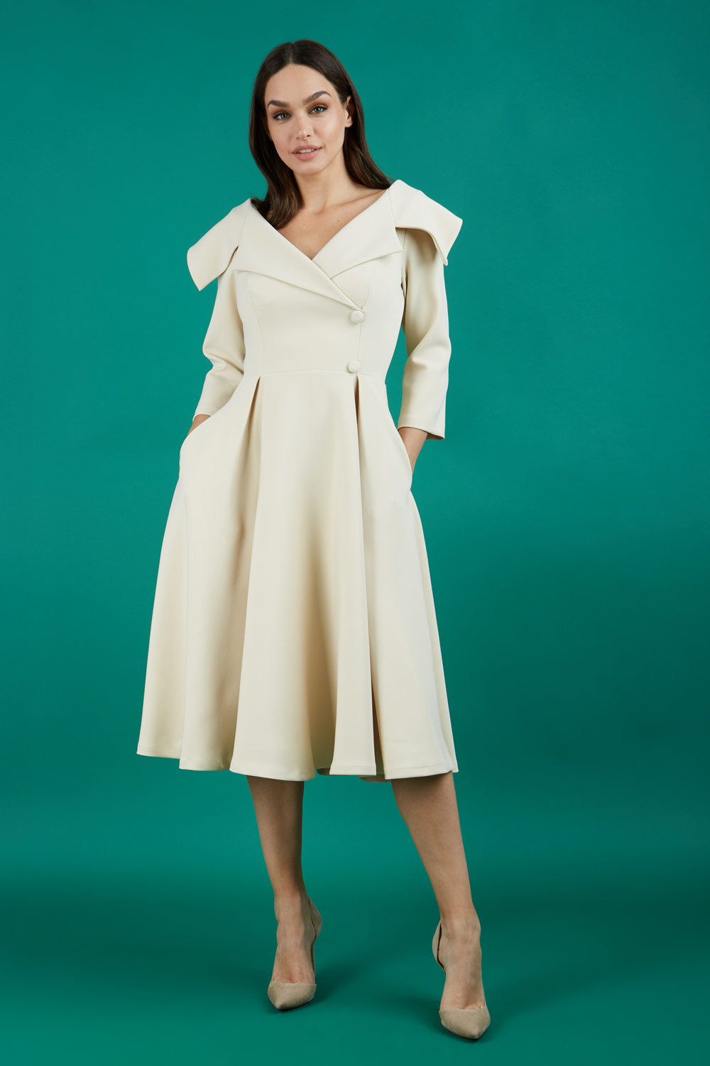 Brunette model is wearing a sleeved beige oversized collar swing dress with button detail at the front and pockets in the skirtmodel is wearing diva catwalk gatsby swing dress with pocket detail and wide v-neck collar and buttons down the front panel in sandshell beige front