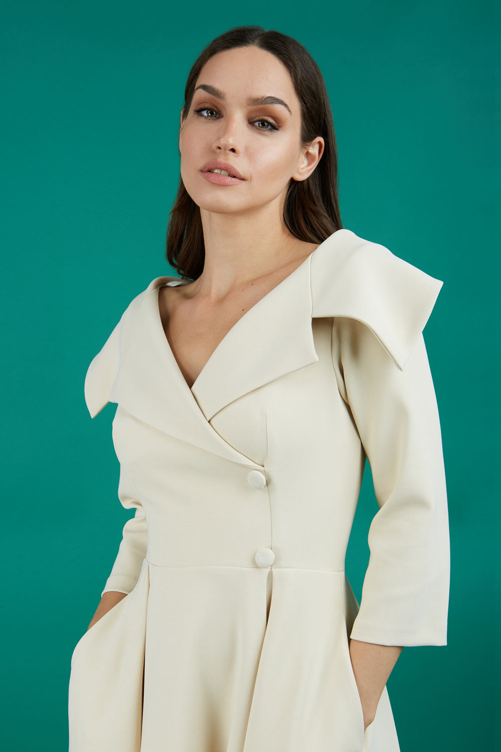 Brunette model is wearing a sleeved beige oversized collar swing dress with button detail at the front and pockets in the skirt