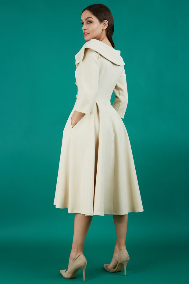 Brunette model is wearing a sleeved beige oversized collar swing dress with button detail at the front and pockets in the skirt back photo