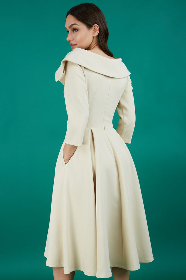 Brunette model is wearing a sleeved beige oversized collar swing dress with button detail at the front and pockets in the skirt