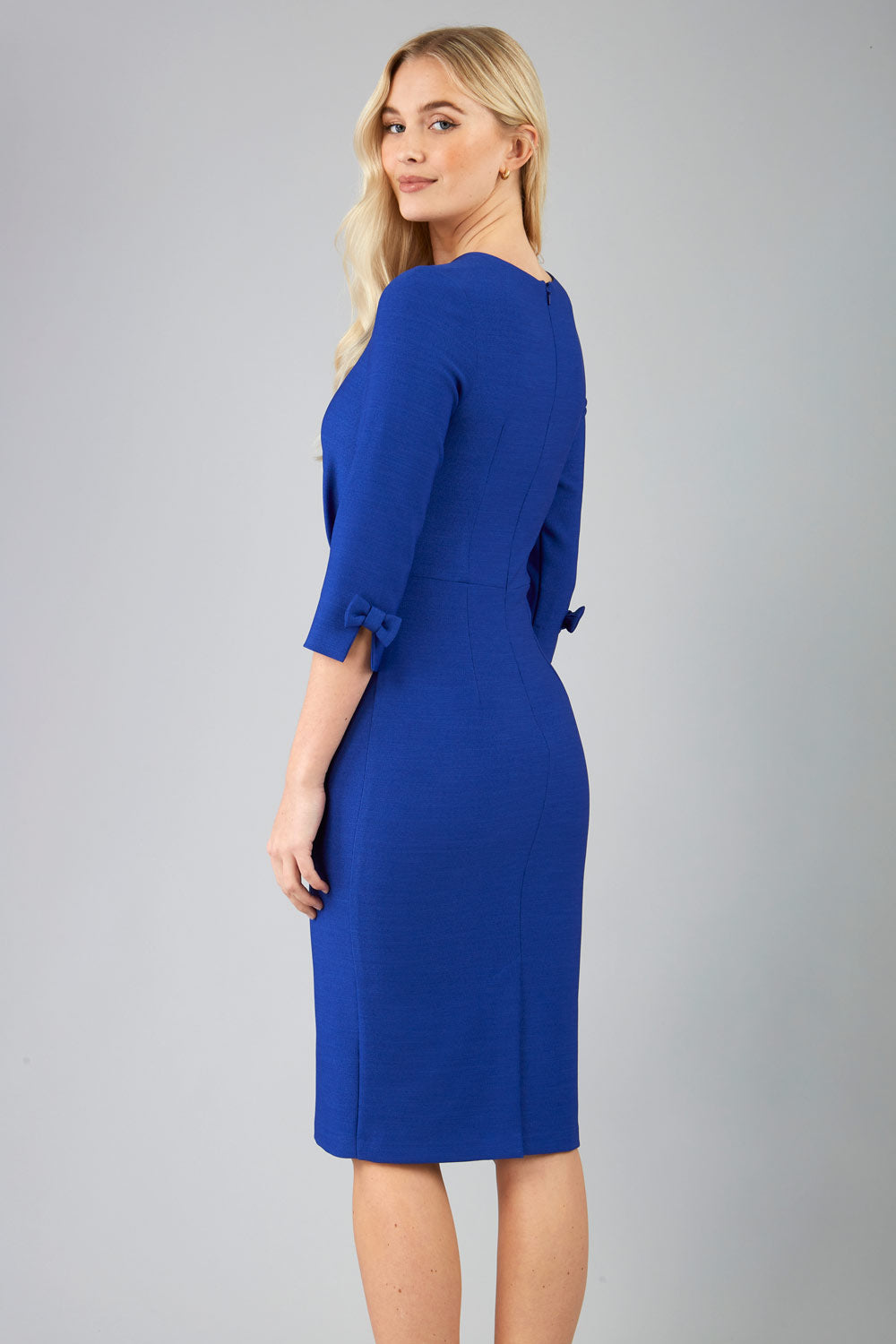 blonde model is wearing diva catwalk logan round neck sleeved pencil dress with side arrow pleating detail in royal blue back