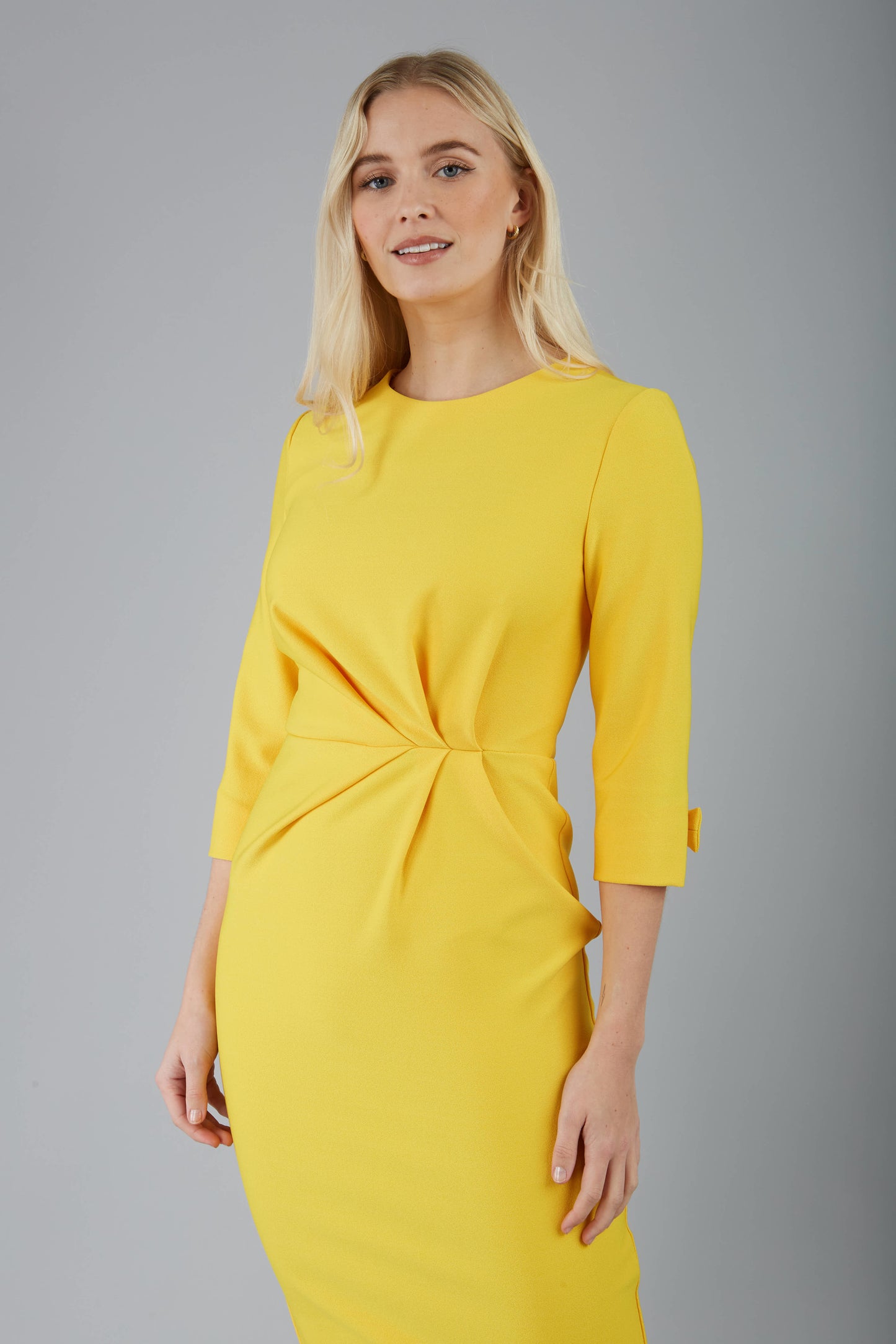 blonde model is wearing diva catwalk logan round neck sleeved pencil dress with side arrow pleating detail in daffodil yellow front