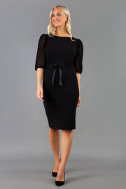 Blonde model is wearing Diva Catwalk Zermatt Lace Short Sleeved Black Pencil skirt Dress with a Belt Detail at the front good for corporate  events and as an office dress or workwear style