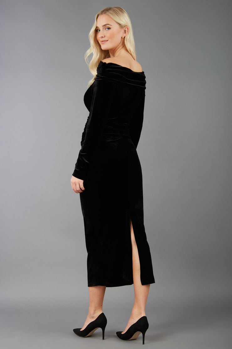 A blonde Model is wearing an off shoulder bardot neckline velvet stretch midi dress in red by diva catwalk back image
