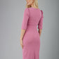 blonde model is wearing diva catwalk lucretis rounded neckline sleeved pencil dress with  rushing on shoulders and rushed detail on a side of a waistline in pink back