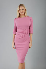 blonde model is wearing diva catwalk lucretis rounded neckline sleeved pencil dress with  rushing on shoulders and rushed detail on a side of a waistline in pink front