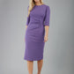 blonde model is wearing diva catwalk lucretis rounded neckline sleeved pencil dress with  rushing on shoulders and rushed detail on a side of a waistline in lavender purple front