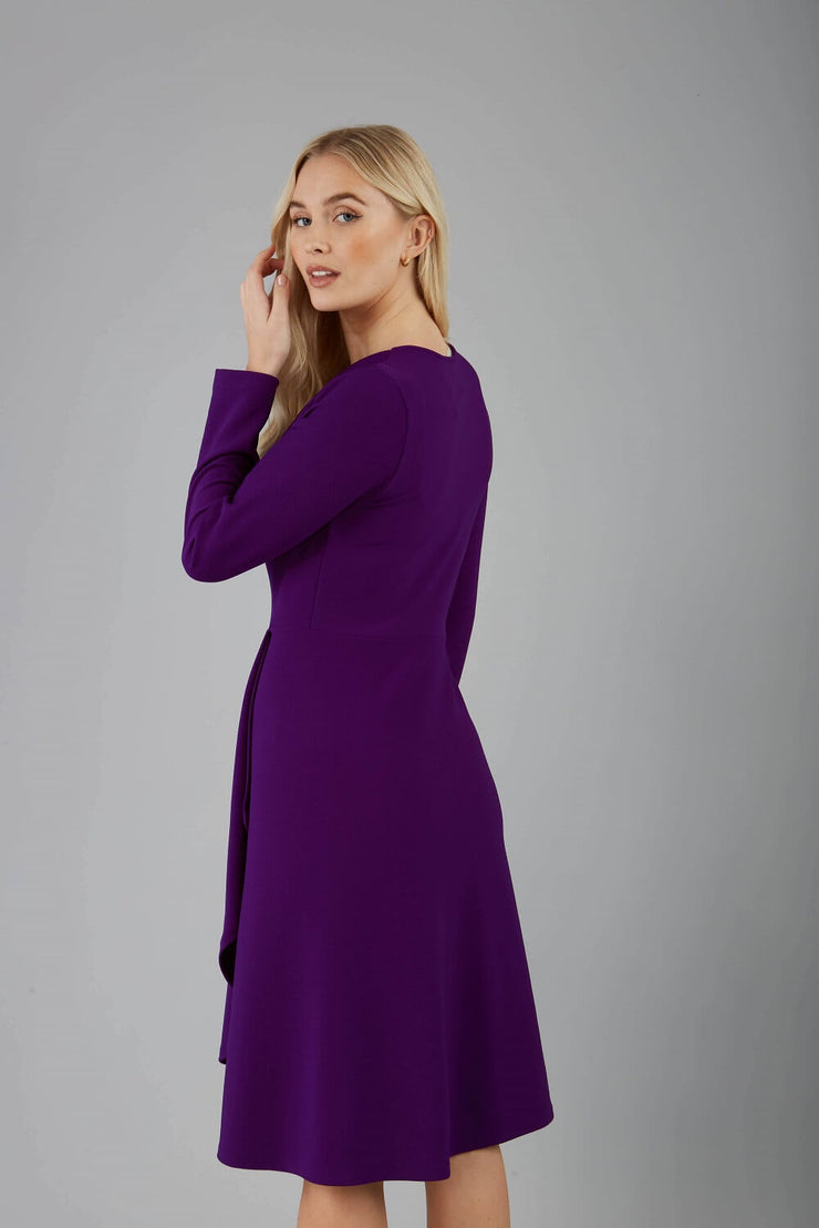 blonde model is wearing diva catwalk moraig swing long sleeve dress with high cowl neckline and wrap skirt in deep purple back