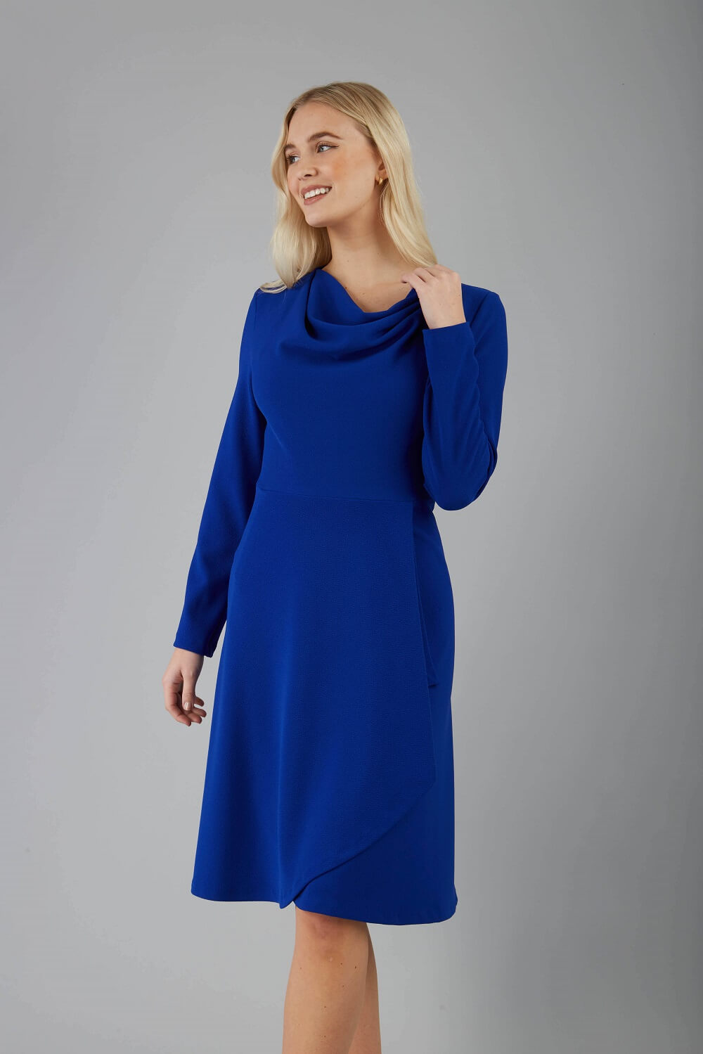 blonde model is wearing diva catwalk moraig swing long sleeve dress with high cowl neckline and wrap skirt in cobalt blue front