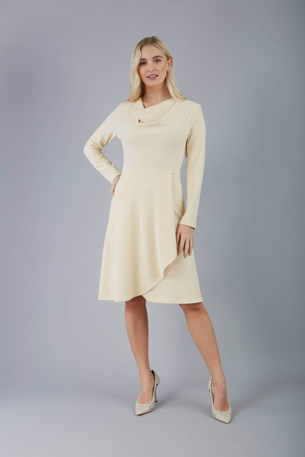 blonde model is wearing diva catwalk moraig swing long sleeve dress with high cowl neckline and wrap skirt in beige front
