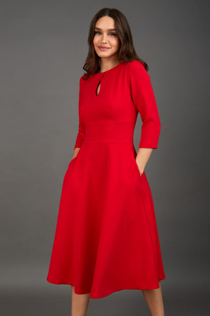 Brunette model is wearing diva catwalk casares swing dress with a keyhole neckline three quarter sleeve dress with pocket detail in red front