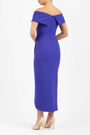 brunette model wearing diva catwalk vegas calf length spectrum indigo midaxi dress with wide bardot neckline and open shoulders with a large opening at the front of the skirt with pleating coming down long skirt back