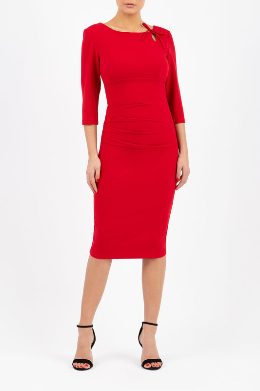 A model is wearing a three quarter sleeve pencil dress with a round neckline and bow detail at the front in red