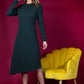 blonde model is wearing diva catwalk dartington asymmetric skirt midaxi long sleeve dress with rounded pleated neckline a-line style in deep green front