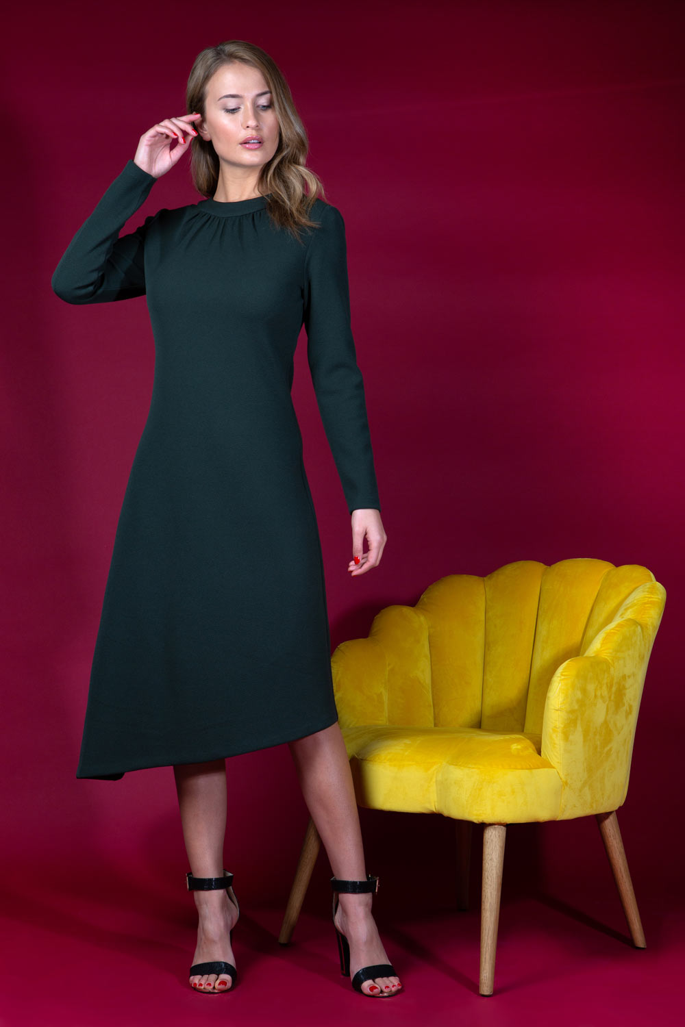 blonde model is wearing diva catwalk dartington asymmetric skirt midaxi long sleeve dress with rounded pleated neckline a-line style in deep green front