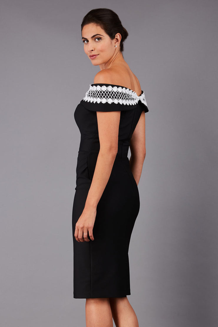 brunette model wearing diva catwalk kurumba pencil dress with bardot off shoulder neckline and lace detail across it in black and white colour back