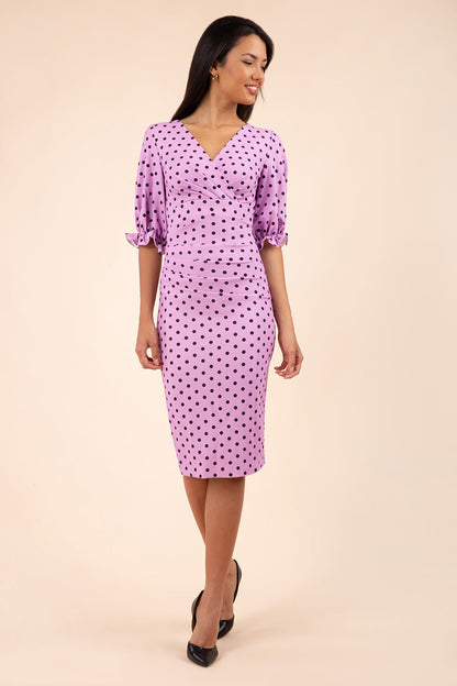 brunette model wearing diva catwalk palacio pencil fitted dress with three quarter puffed sleeve and pleating across the body with overlapping v-neckline in pink polka dot front