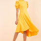 brunette model wearing diva catwalk ola swing dress with puffed oversized sleeves and asymmetric swing skirt with rounded high neck in yellow front