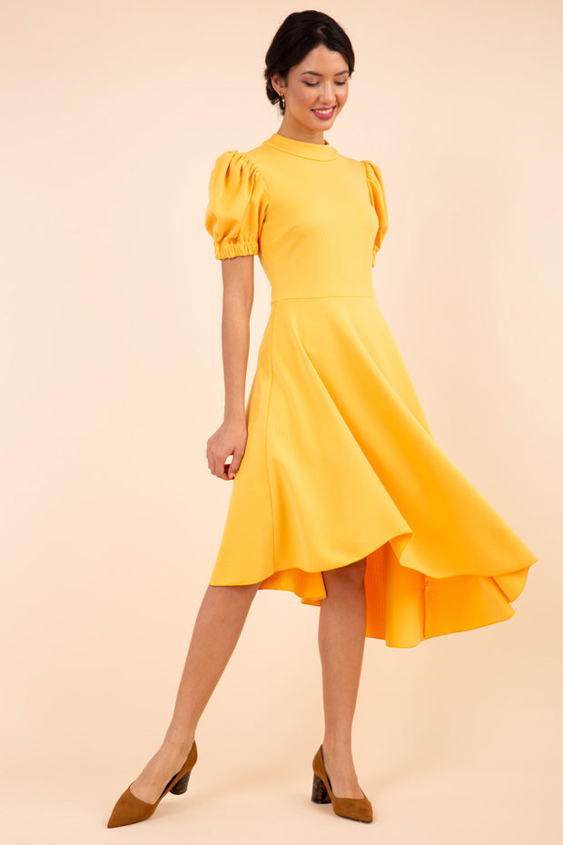 brunette model wearing diva catwalk ola swing dress with puffed oversized sleeves and asymmetric swing skirt with rounded high neck in yellow front