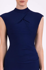 brunette model wearing diva catwalk beyonce pencil fitted dress with high neckline without sleeves with a wide band and pleating across the tummy area with a crossed detail neckline in navy blue  front