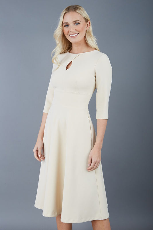 Brunette model is wearing diva catwalk casares swing dress with a keyhole neckline three quarter sleeve dress with pocket detail in sandshell beige front