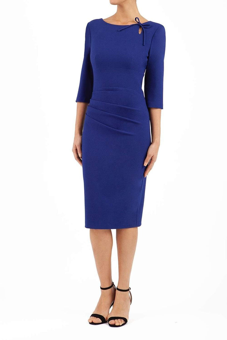 A model is wearing a three quarter sleeve pencil dress with a round neckline and bow detail at the front in oxford blue