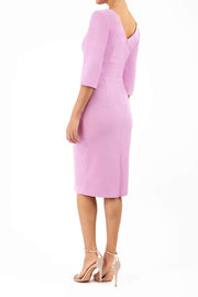 A model is wearing a three quarter sleeve pencil dress with a round neckline and bow detail at the front in pink